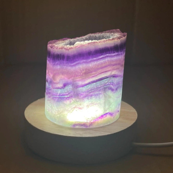 Stunning Rainbow Fluorite Crystal Light Lamp with mesmerizing purple, green, and clear bands, illuminated on a wooden base.