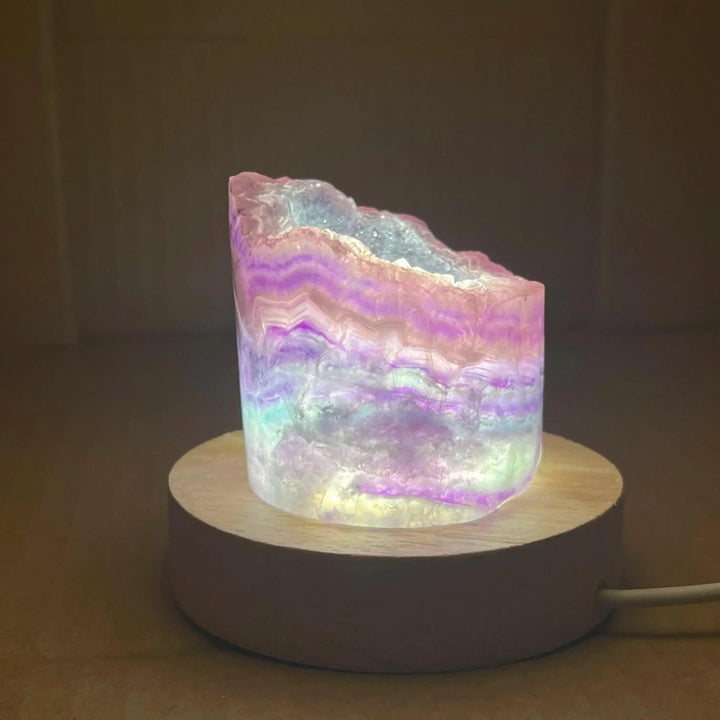Rainbow Fluorite Crystal Light Lamp with mesmerizing purple, green, and blue bands, illuminated on a wooden base.
