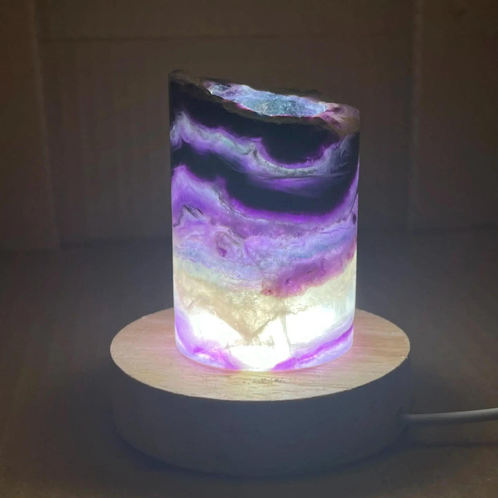 Rainbow Fluorite Crystal Light Lamp with mesmerizing purple, green, and clear bands, illuminated on a wooden base.