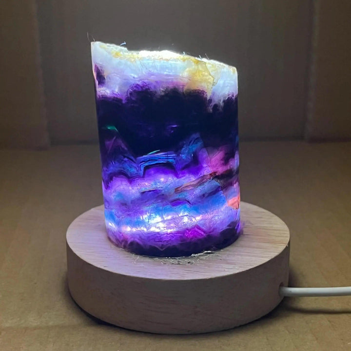 Rainbow Fluorite Crystal Light Lamp with mesmerizing purple, blue, and clear bands on a wooden base, creating a soft, ambient glow.