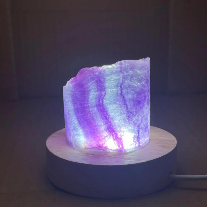 Rainbow Fluorite Crystal Light Lamp with glowing purple and white bands on a wooden base.