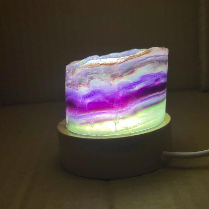 Rainbow Fluorite Crystal Light Lamp with mesmerizing purple, green, and clear bands, illuminated on a wooden base.
