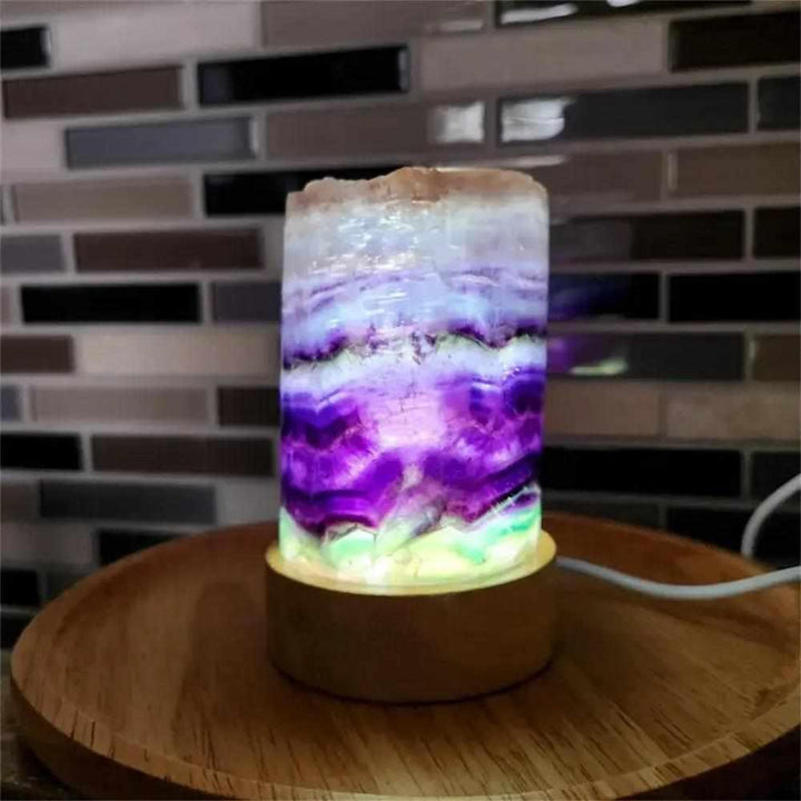 Polished rainbow fluorite crystal lamp with vibrant purple and green banding on a wooden base for meditation and decor.