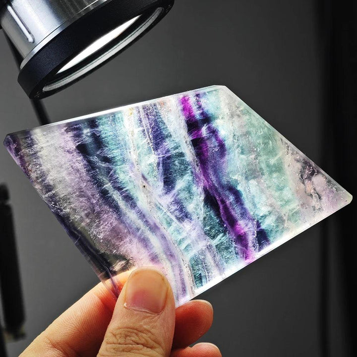 Translucent rainbow fluorite slice featuring vibrant purple and green bands, perfect for reiki healing and home decor.