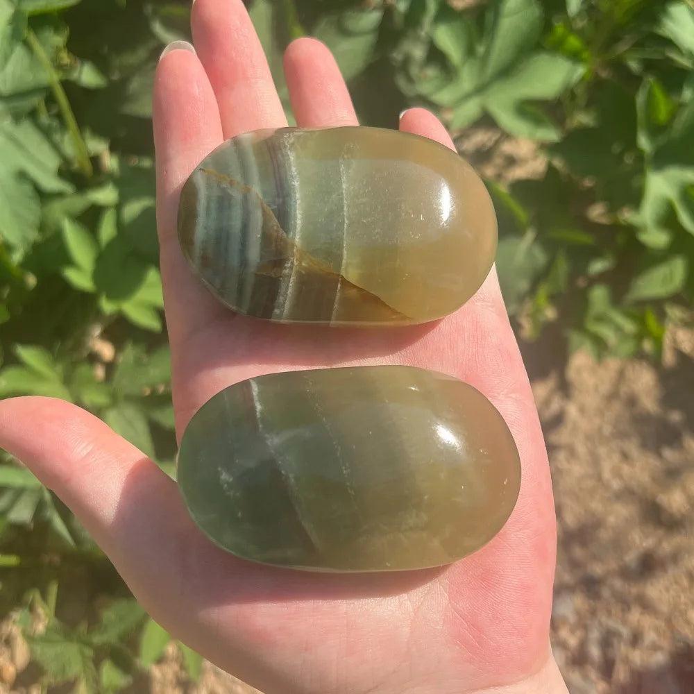 Two smooth, polished green and brown Mango Fluorite healing crystal palm stones held in a hand.