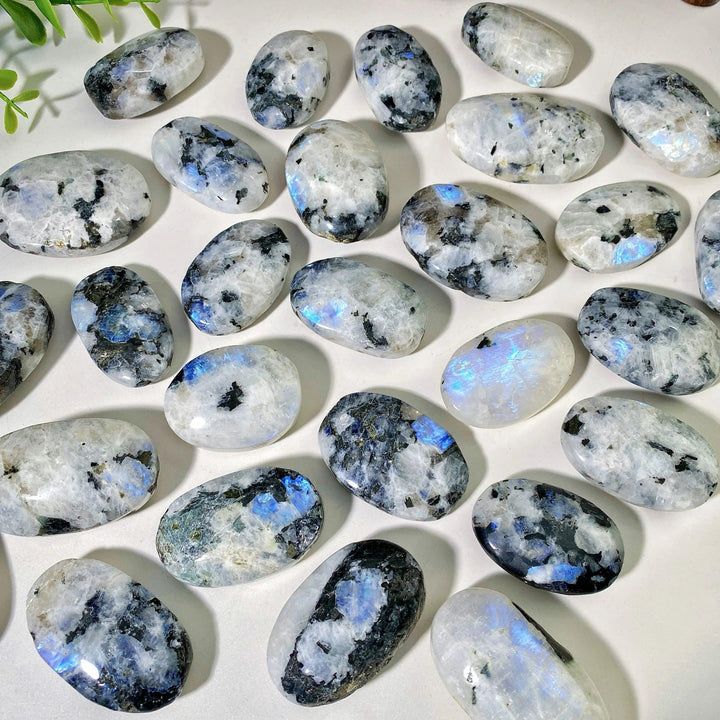 Polished Rainbow Moonstone palm stones with shimmering blue flashes and natural black inclusions for healing decor.
