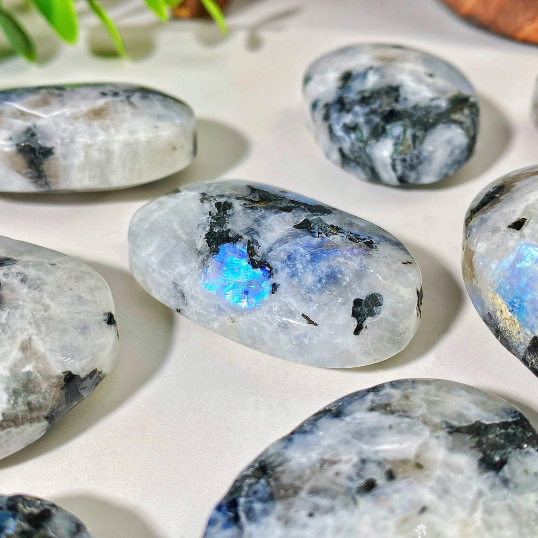 Polished rainbow moonstone palm stone featuring iridescent blue flashes and natural mineral inclusions for healing.