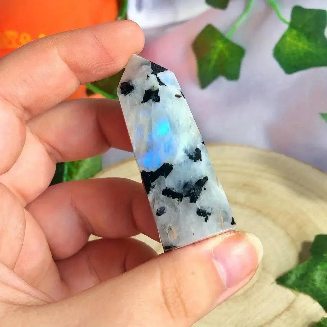 Hand holding a Rainbow Moonstone crystal tower with iridescent blue flashes and black inclusions from Crystal Destiny.