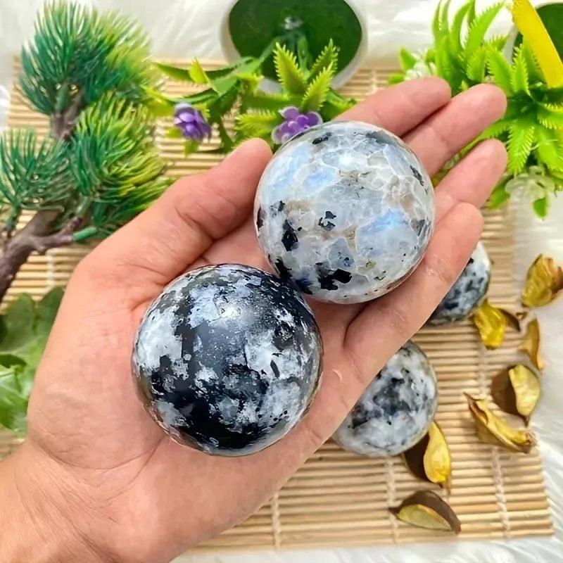 Hand holding two luminous Rainbow Moonstone spheres from Crystal Destiny, displaying blue and white flashes.
