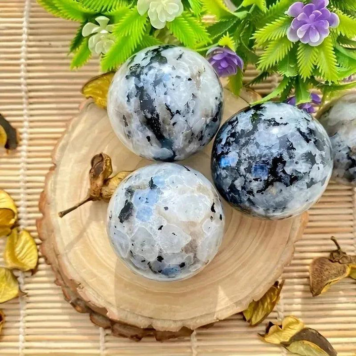 Three polished Rainbow Moonstone spheres with blue flashes on a wooden slice, from Crystal Destiny.