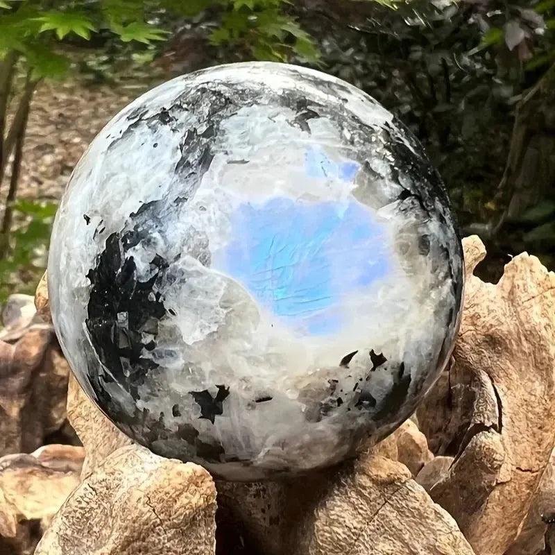 Luminous Rainbow Moonstone sphere from Crystal Destiny, displaying blue and rainbow adularescence on a natural wood base.