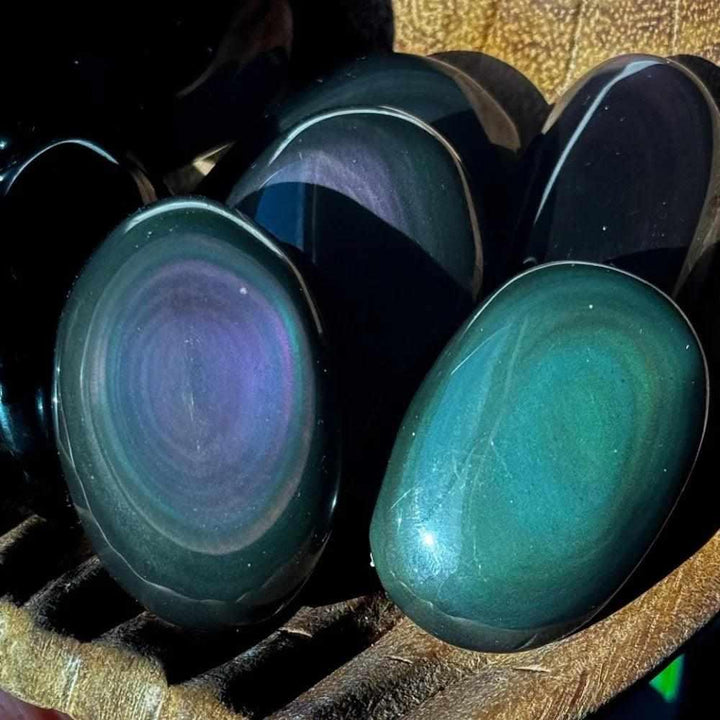 Smooth Rainbow Obsidian palm stone with a glossy black finish and vibrant purple and gold sheen for grounding and protection.
