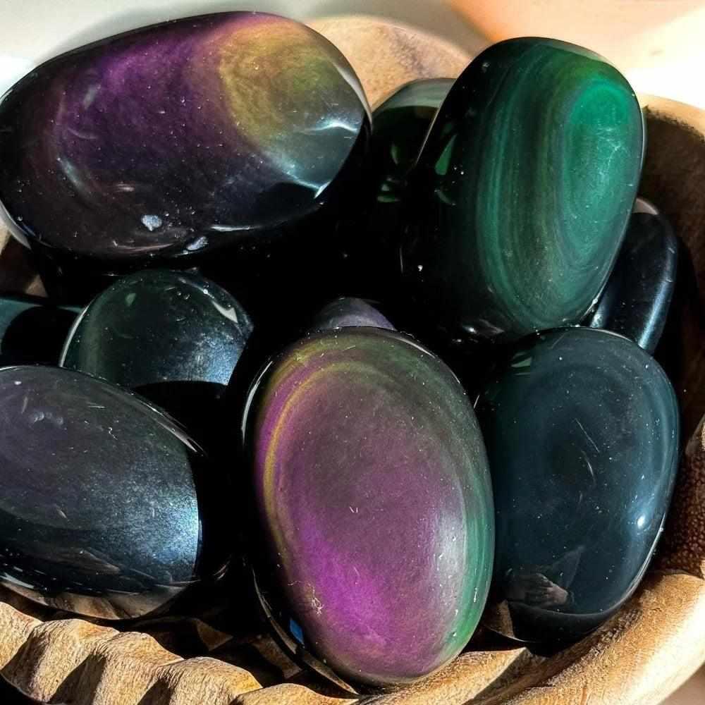 Glossy Rainbow Obsidian palm stones with shimmering purple, green, and gold bands for grounding and protection.