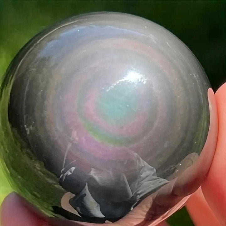 Polished Rainbow Obsidian sphere showing vibrant iridescent bands for root chakra protection and self-reflection.