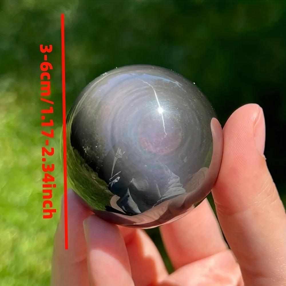 Polished Rainbow Obsidian sphere showing black volcanic glass with a subtle rainbow sheen, held for scale, 30-50mm size.