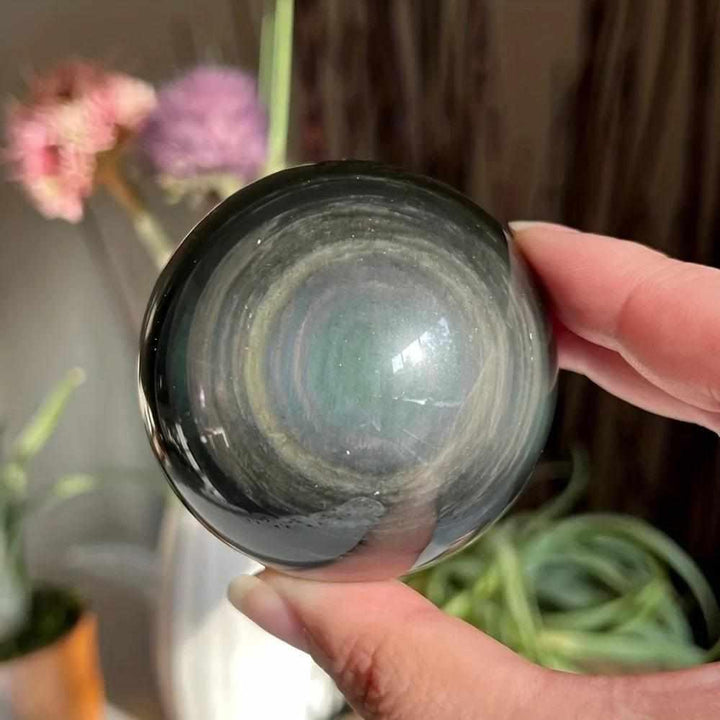 Polished Rainbow Obsidian sphere showing black volcanic glass with shimmering rainbow bands for root chakra protection.