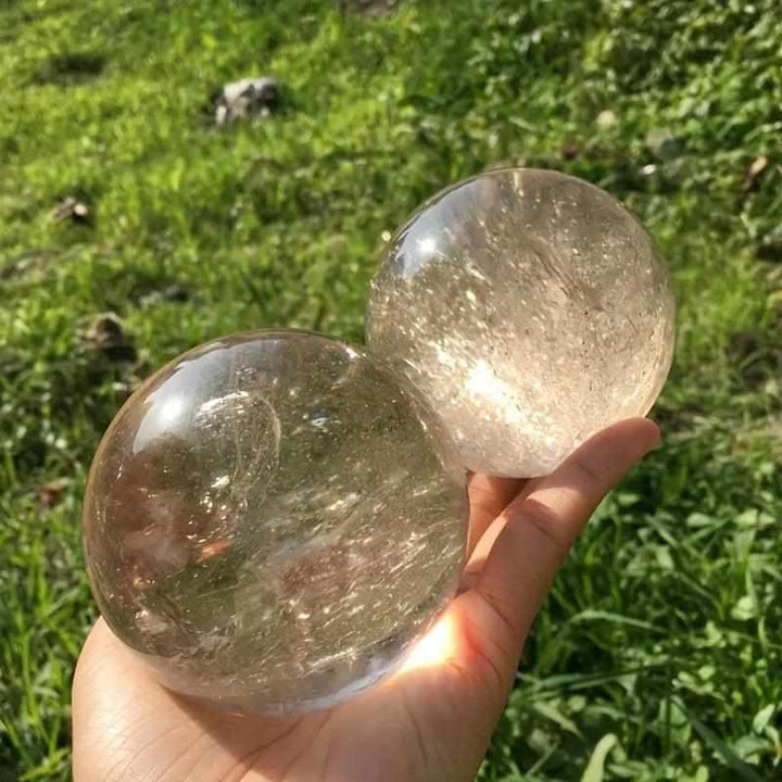 Two polished Rainbow Smoky Quartz spheres held in hand, showing translucent brown tones and natural internal rainbows.