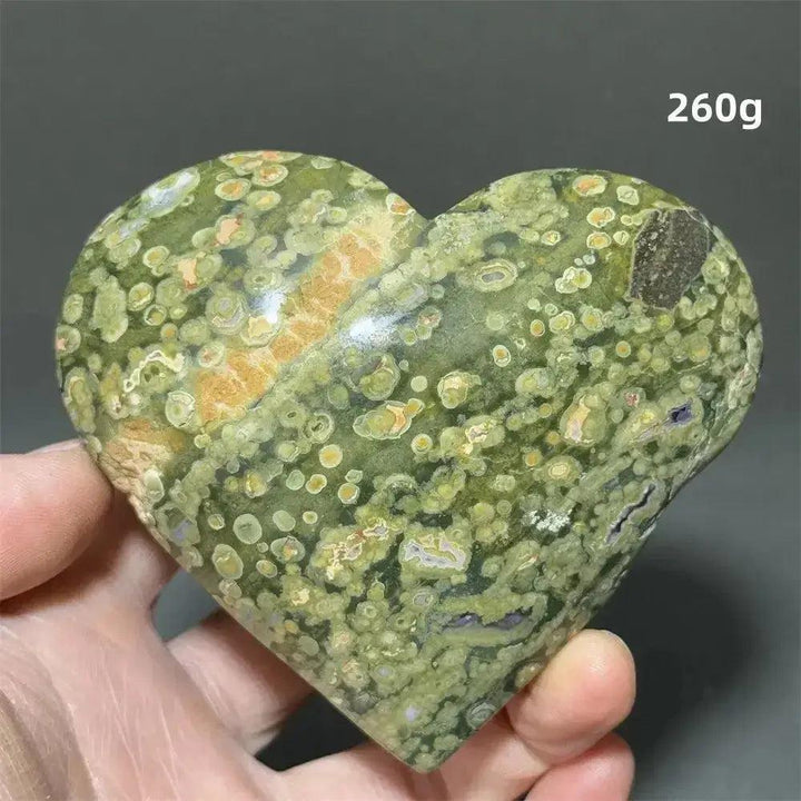 Rainforest Jasper heart crystal, 260g, with green, orange, and brown patterns, held in a hand. Crystal Destiny.