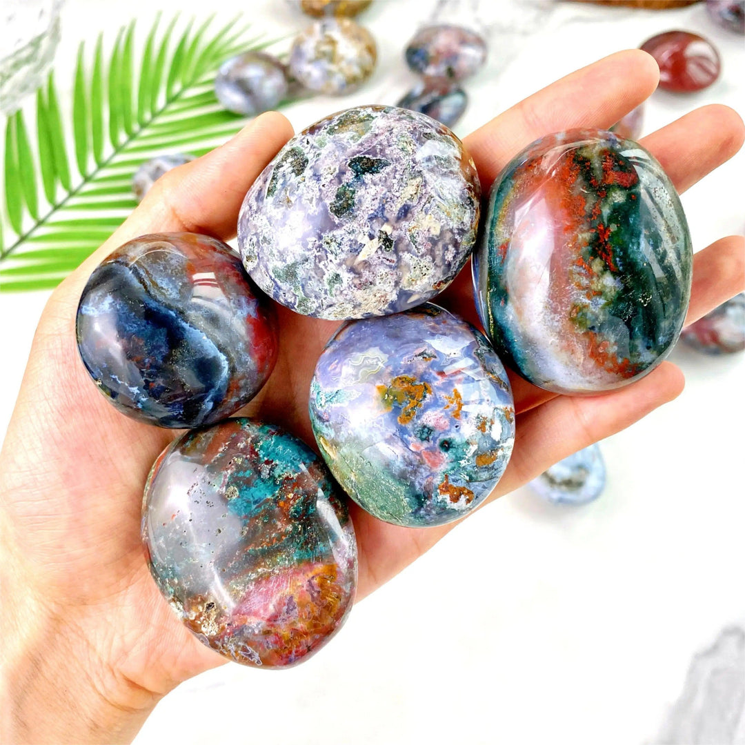 Hand holding polished Ocean Jasper palm stones with vibrant, multicolored natural patterns for healing and decoration.