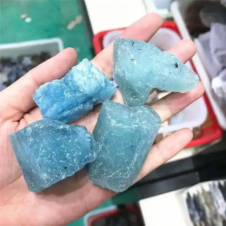 Handheld raw aquamarine stones featuring natural sea-blue hues, rough textures, and calming energy for crystal healing.