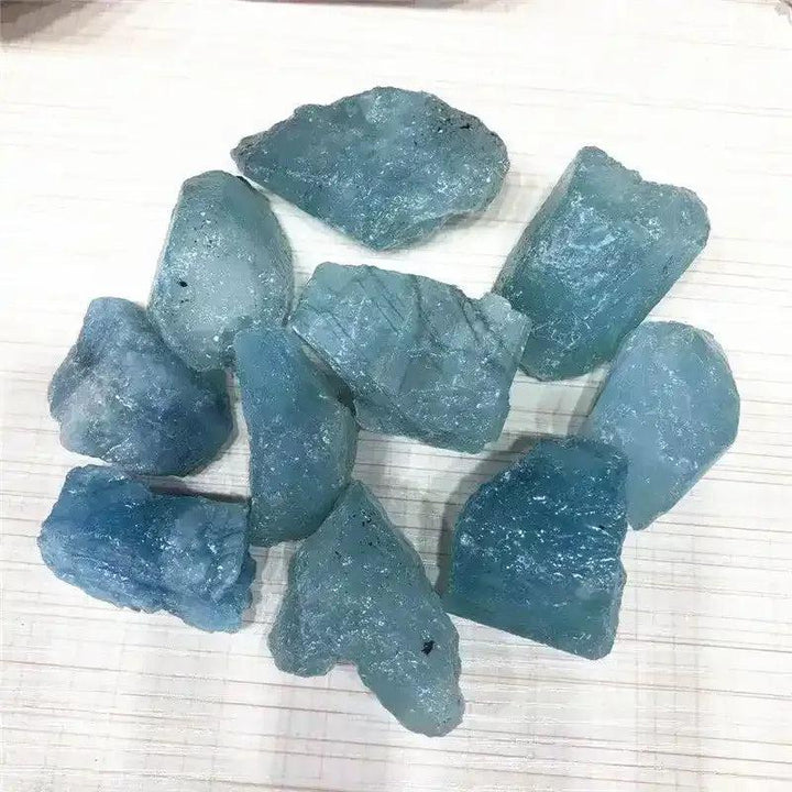 Raw aquamarine stones in cool sea blue, featuring natural rough textures and inclusions for Throat and Heart chakra healing.