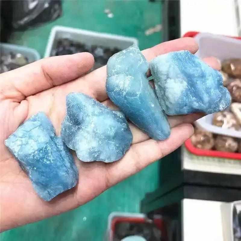 Handheld raw aquamarine stones featuring natural sea-blue hues, rough textures, and calming energy for chakra healing.