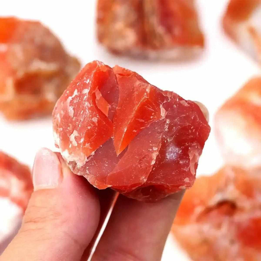 Hand holding a raw, unpolished Carnelian stone with vibrant orange-red hues, perfect for sacral chakra energy and courage.