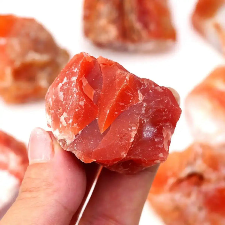 Hand holding a raw, unpolished Carnelian stone with vibrant orange-red hues, perfect for sacral chakra energy and courage.
