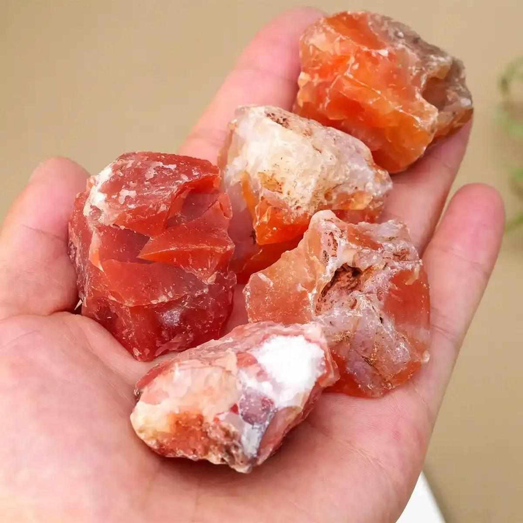 Hand holding raw Carnelian stones with vibrant orange and red-brown hues, perfect for Sacral and Root chakra energy.