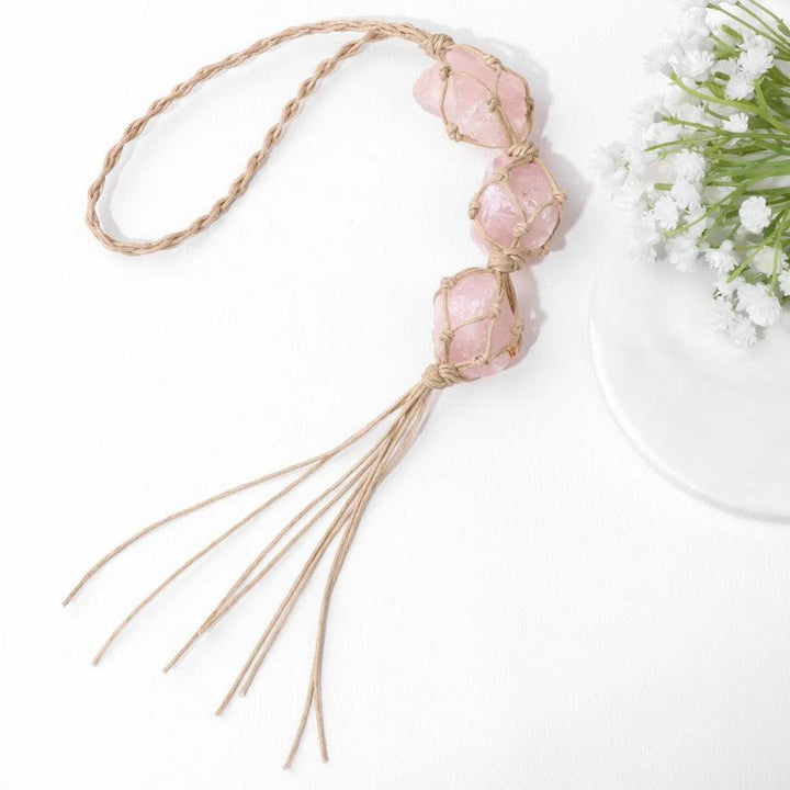 Three raw pink rose quartz stones in macrame net, hanging from a braided twine loop, with tassels.