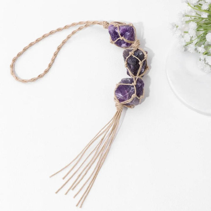Irregular raw amethyst stones in a macrame car pendant, promoting calm and spiritual growth.