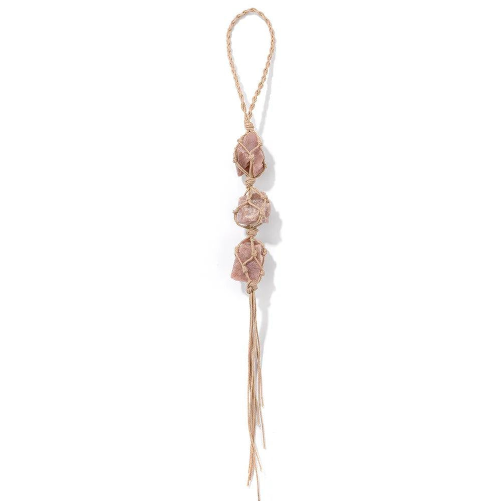 Three irregular raw pink quartz stones in macrame, hanging as a car rearview mirror pendant for interior decoration.