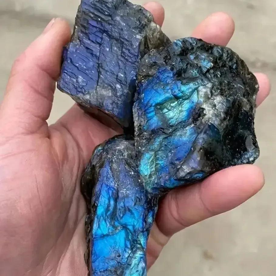 Hand holding raw Labradorite rough crystals with vibrant blue and green labradorescence from Crystal Destiny.