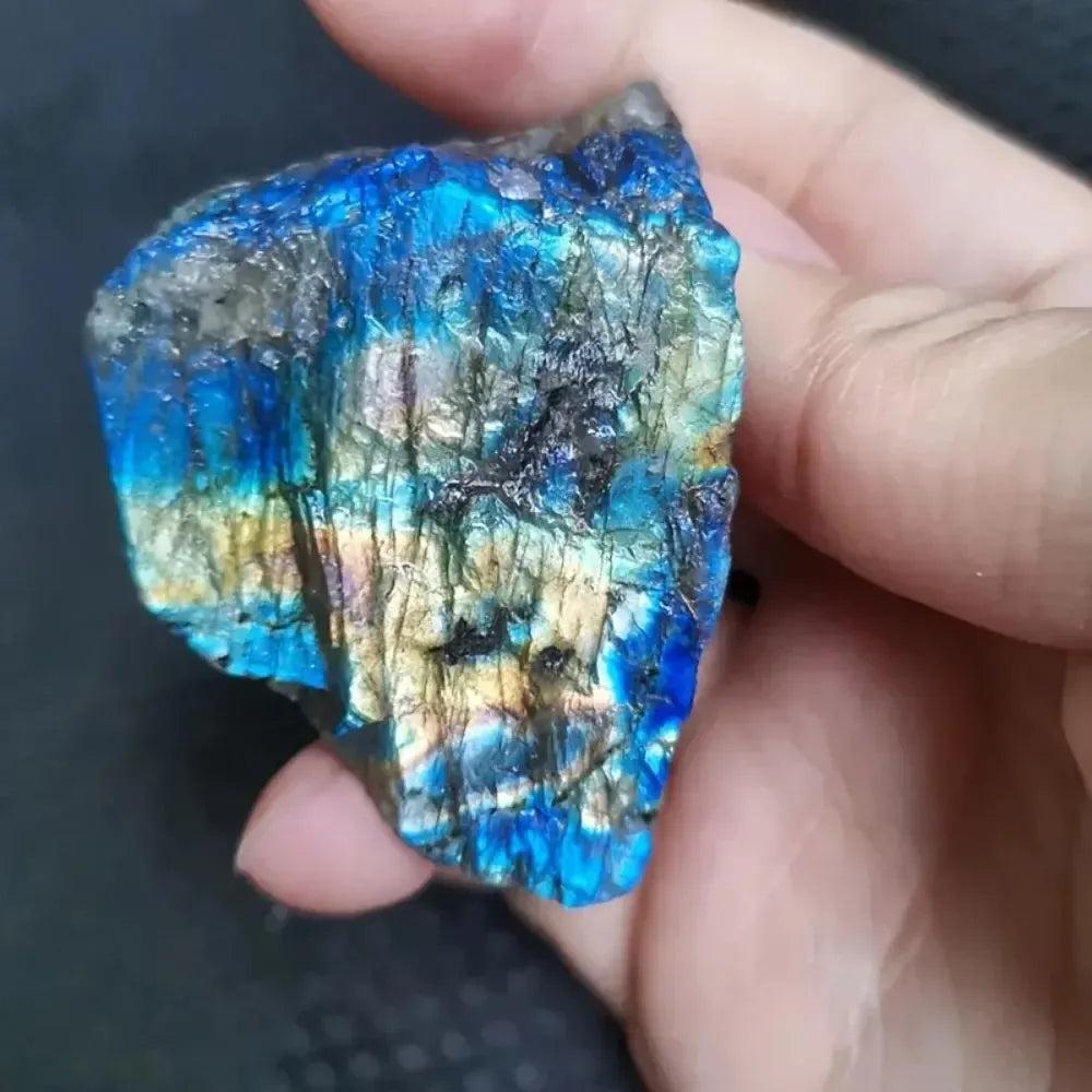 Hand holding a raw Labradorite rough crystal with vibrant blue, green, and gold flashes from Crystal Destiny.