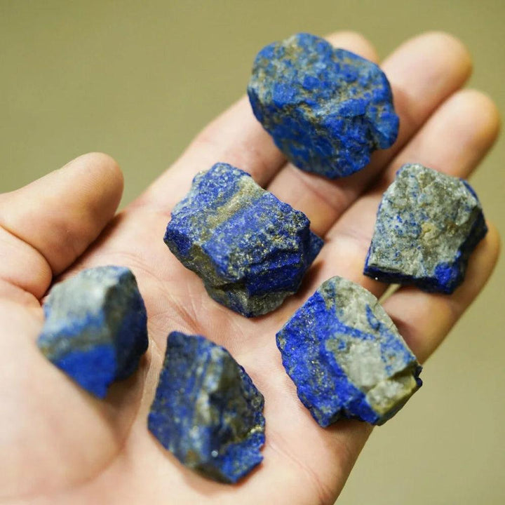 Raw Lapis Lazuli stones with deep blue color and golden pyrite flecks held in a hand for chakra healing and meditation.