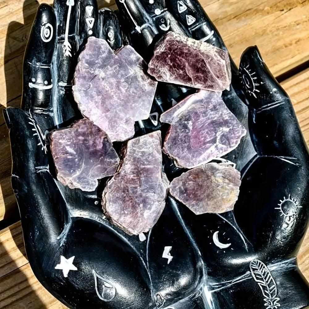 Raw Lepidolite slices with glittering purple mica, resting in a black celestial hand dish for calming energy and balance.