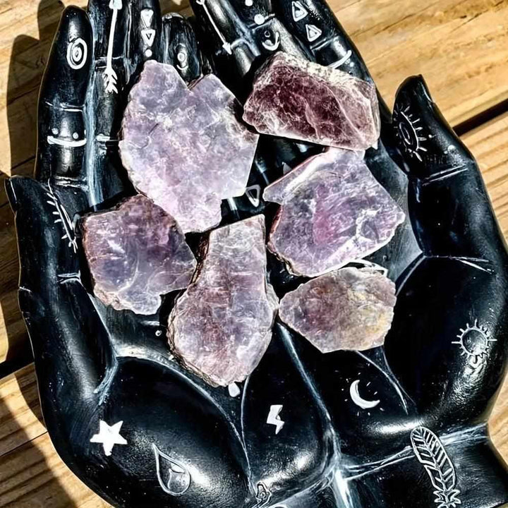 Raw Lepidolite slices with glittering purple mica, resting in a black celestial hand dish for calming energy and balance.