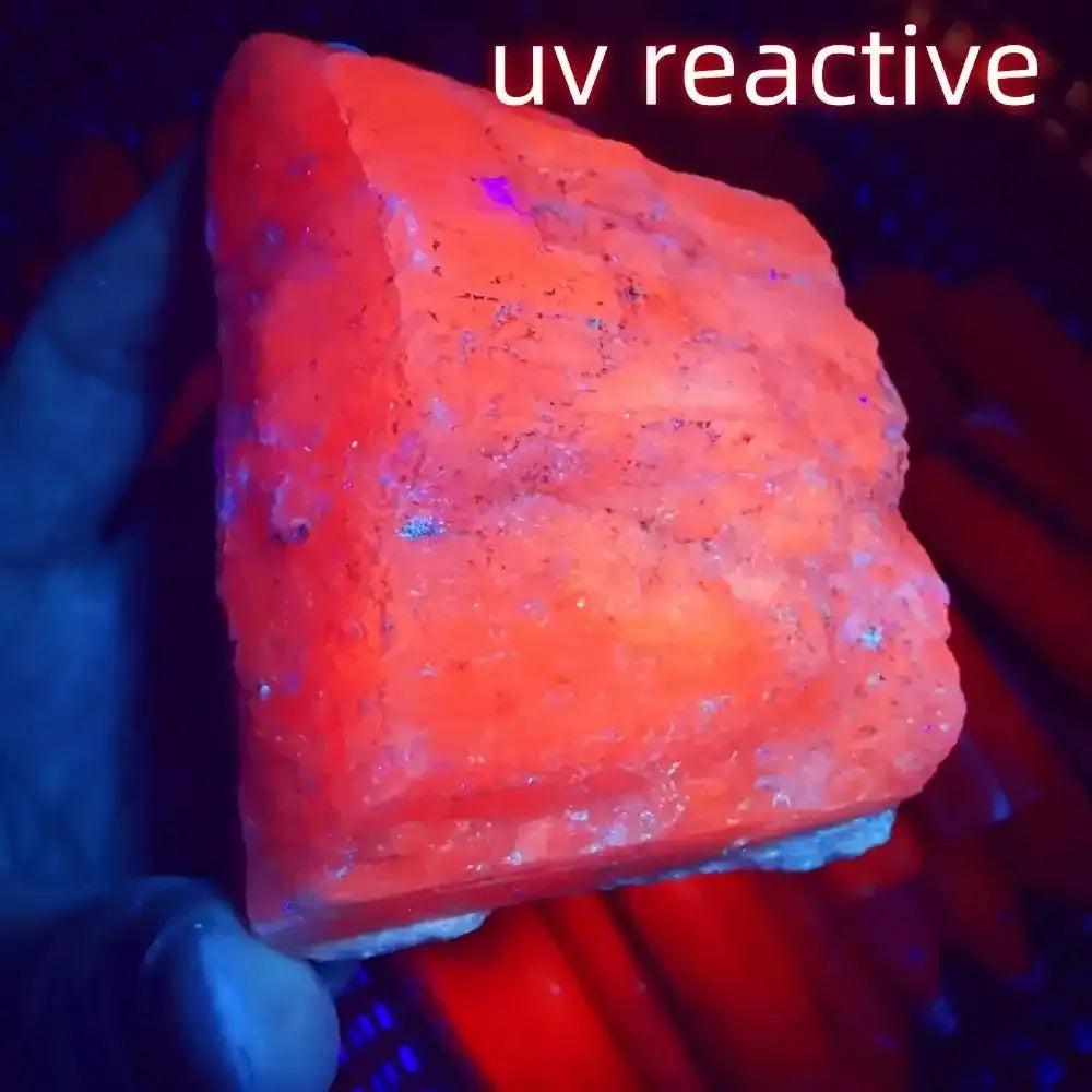 Raw pink Kunzite stone glowing with a vibrant orange UV reactive finish, perfect for Heart chakra healing and meditation.