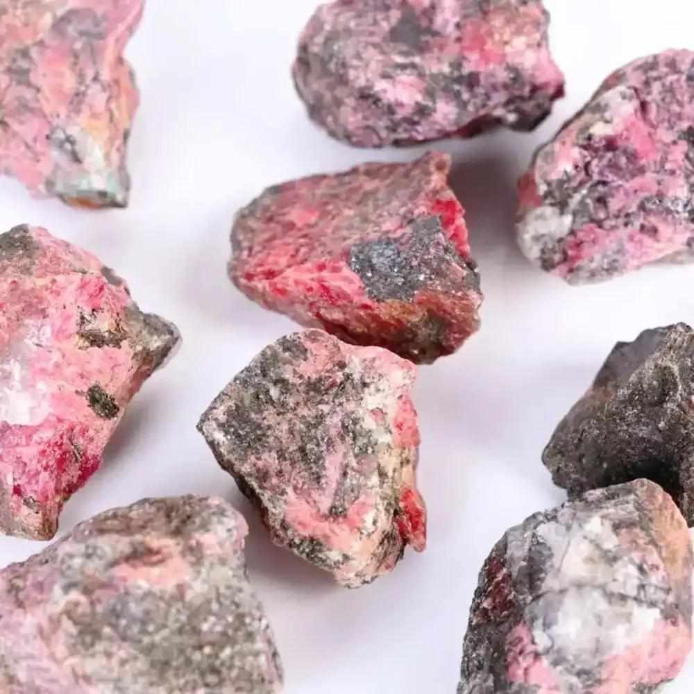 Raw Rhodonite stones featuring rosy pink hues and natural black veins for Heart chakra healing and emotional balance.