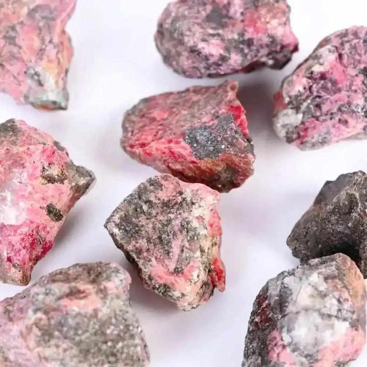 Raw Rhodonite stones featuring rosy pink hues and natural black veins for Heart chakra healing and emotional balance.