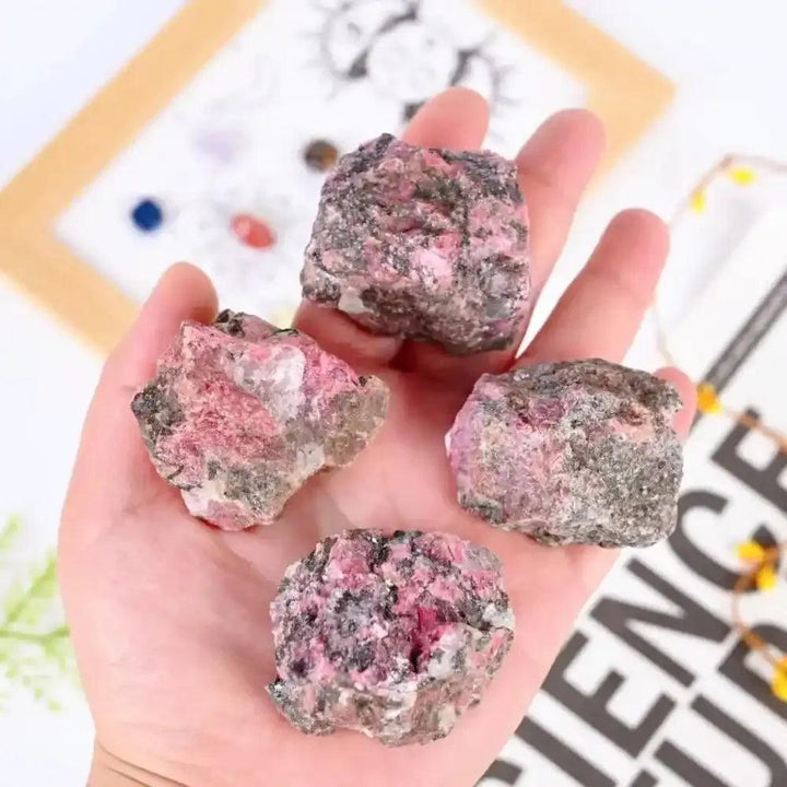 Handheld raw rhodonite stones featuring rosy pink hues and natural black veins for heart chakra healing and balance.