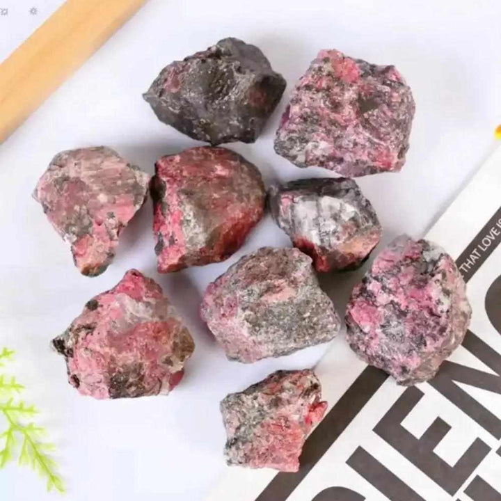 Raw rhodonite stones featuring rosy pink hues and black veins, perfect for Heart chakra healing and emotional balance.