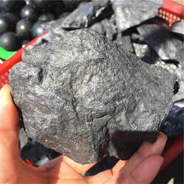 Handheld raw Shungite stone featuring a matte black, unpolished texture for natural root chakra protection and grounding.