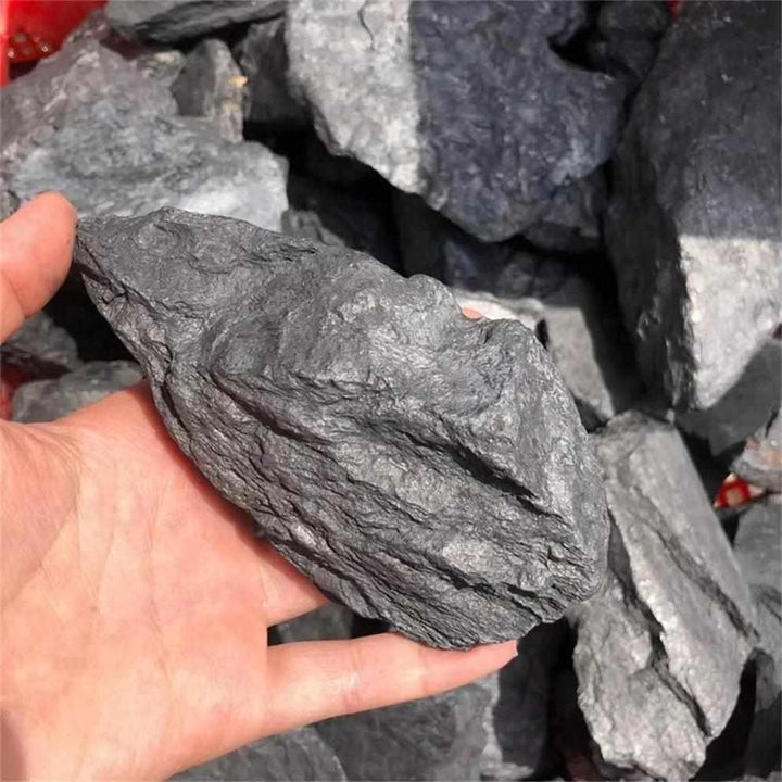 Hand holding a raw, matte black Shungite stone from Russia, perfect for root chakra protection and home purification.
