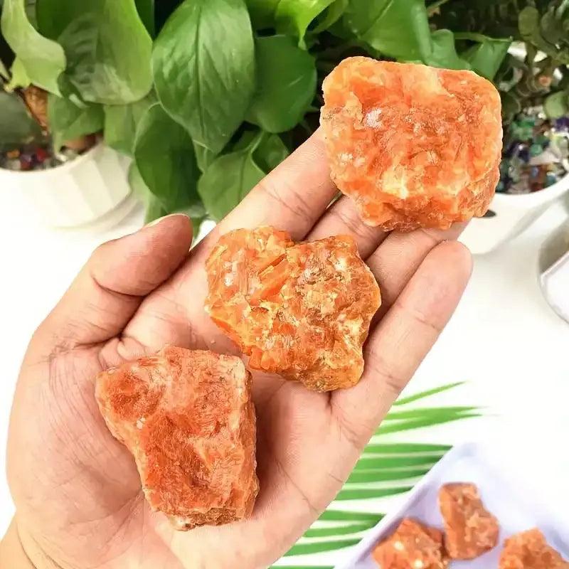 Hand holding three raw Sunstone chunks with warm orange, glittery textures for Sacral and Solar Plexus chakra healing.