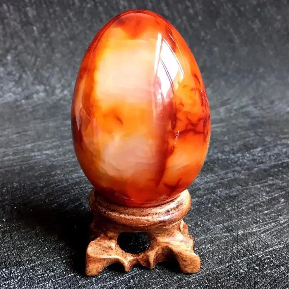 Polished Red Agate Crystal Egg, vibrant crimson to orange, on a carved wooden stand. Grounding Root Chakra.