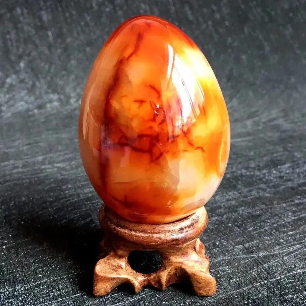 Polished Red Agate Crystal Egg, vibrant deep crimson to warm cream banding, on a wooden stand for grounding Root Chakra.