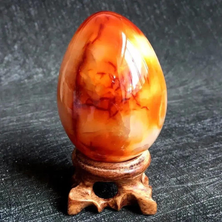 Polished Red Agate Crystal Egg, vibrant deep crimson to warm cream banding, on a wooden stand for grounding Root Chakra.