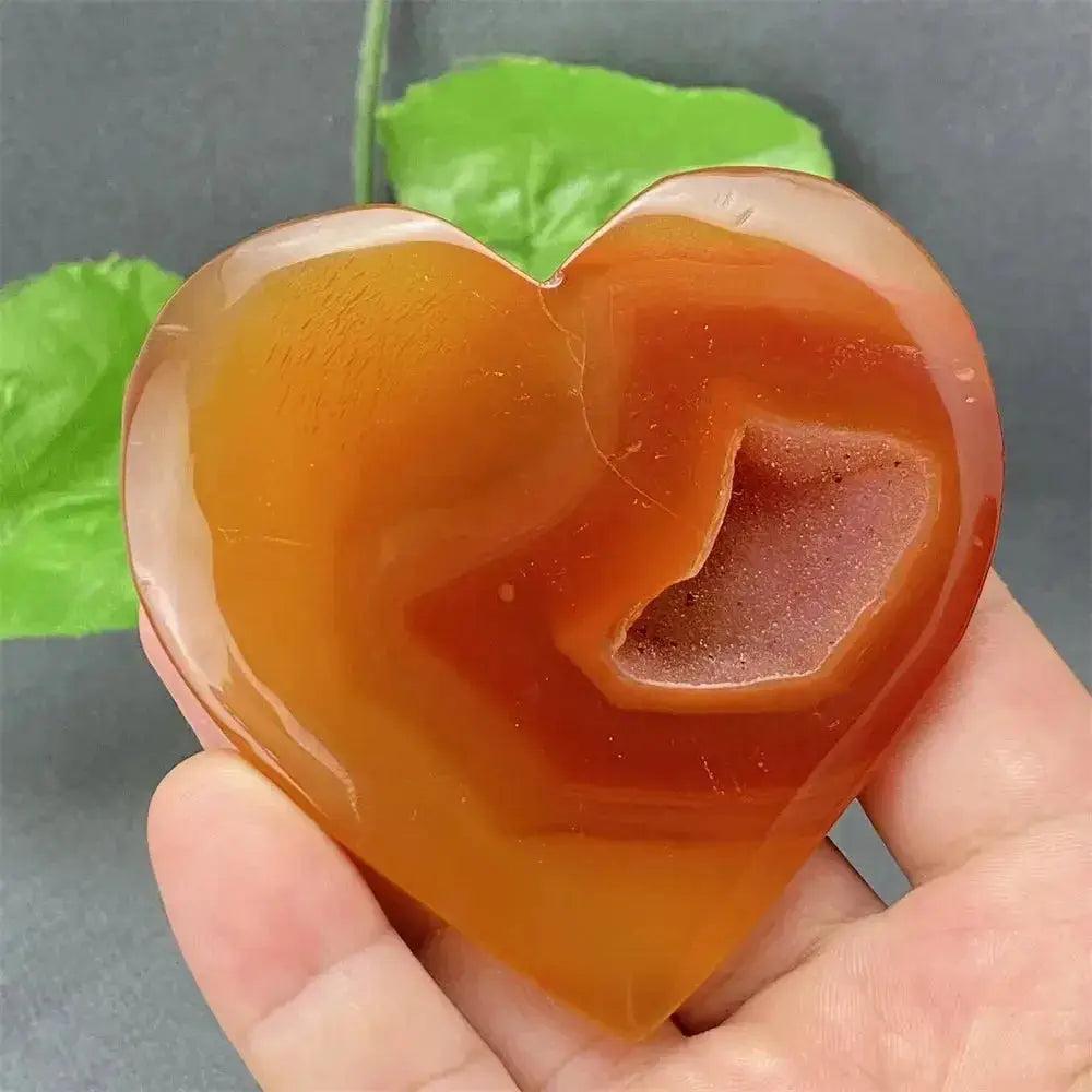Natural Red Agate Heart Geode, polished exterior with sparkling druzy crystals, held in hand.