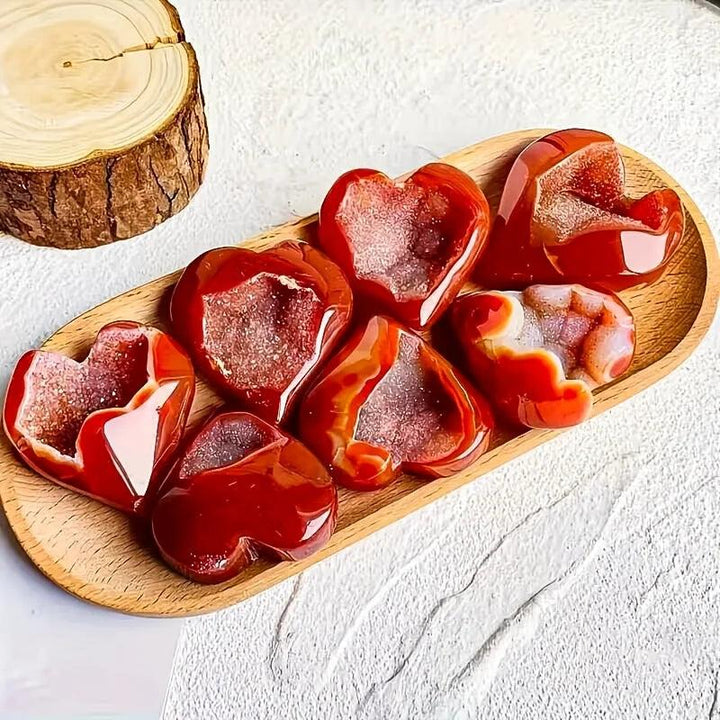 Polished red agate heart-shaped stones with sparkling natural crystal druzy centers on a wooden tray.